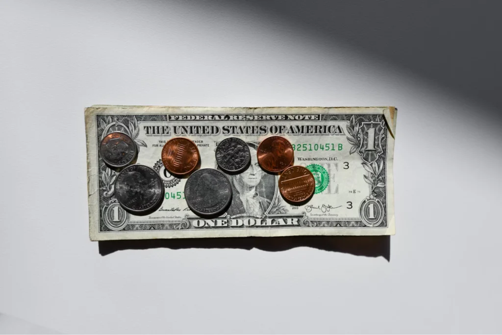 Various coins and a U.S. dollar bill arranged on a white surface.