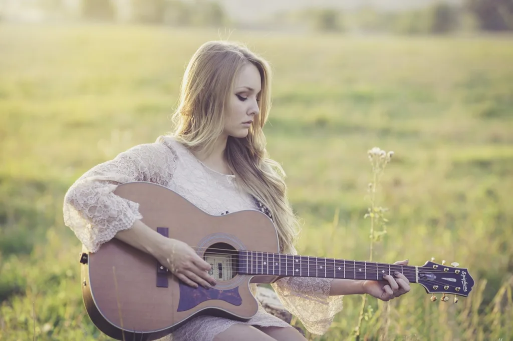 A woman sitting outdoors in a grassy field playing an acoustic guitar.