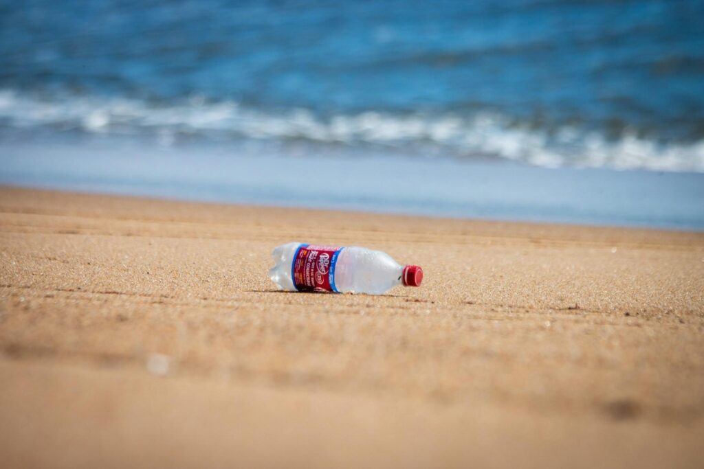 A plastic bottle discarded on a sandy beach, with ocean waves in the background.