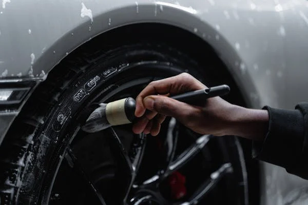 Close-up of a hand cleaning a car tire with a brush that is covered in soap suds.