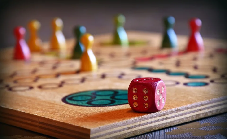 Close-up of a board game with colorful playing pieces and a red dice on a wooden board.