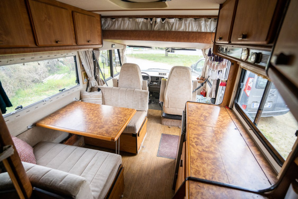 Interior of a motorhome showing a cozy seating area with tables, cabinets, and driver seats.