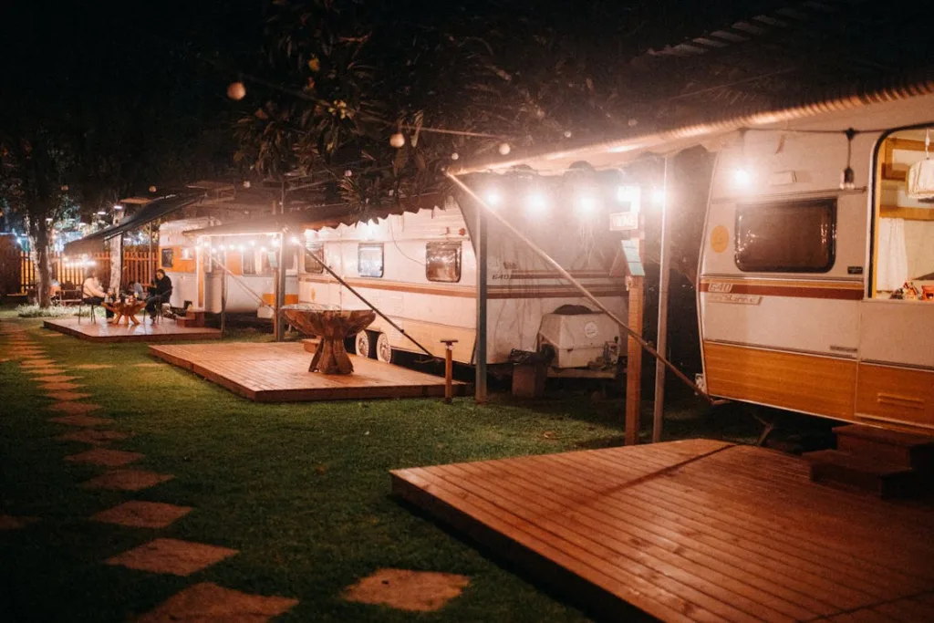 A night scene of several well-lit RVs parked in a row at a campground.