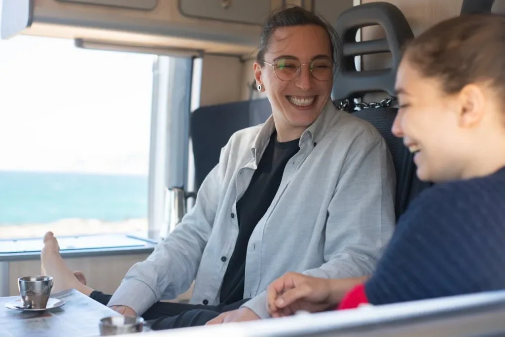 Two women sitting inside a camper van, smiling and having a conversation over tea.