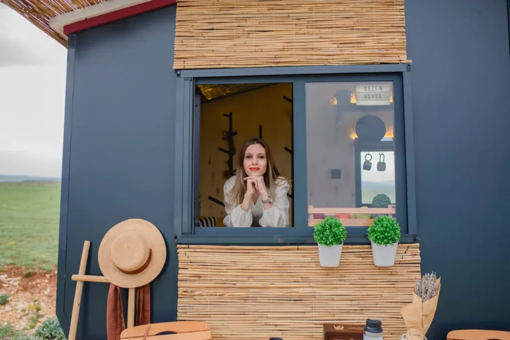 A woman leaning out of a window of a small house-like structure, resting her chin on her hands.