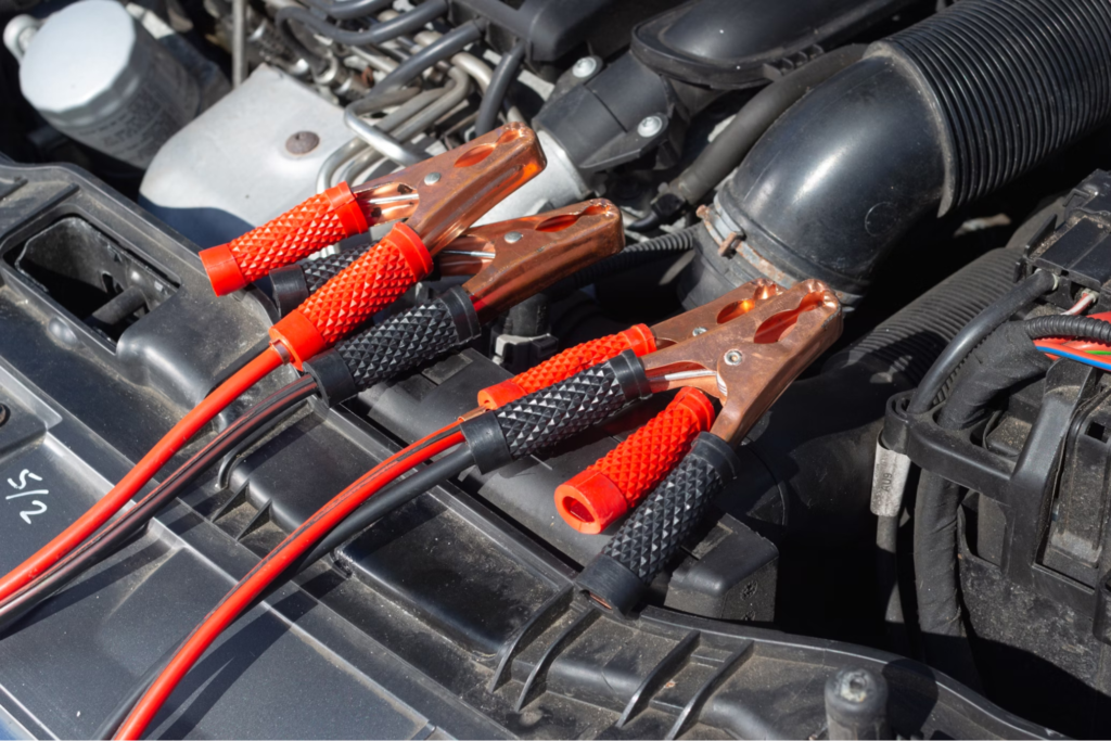 Jumper cables connected to a car battery under the hood of a vehicle.