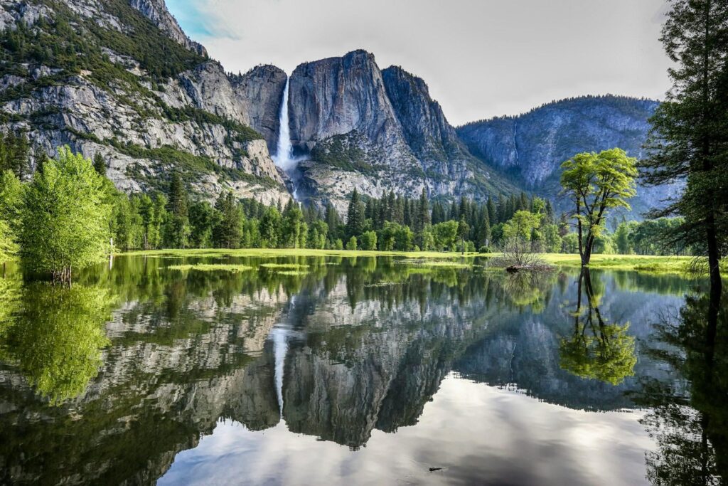 A scenic view of a tranquil lake reflecting surrounding trees and mountains, under a partly cloudy sky.