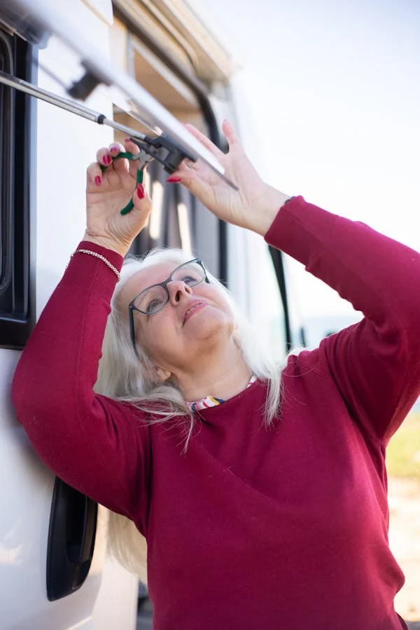 An older woman in a red sweatshirt adjusting the awning latch on a campervan, seen in close-up.