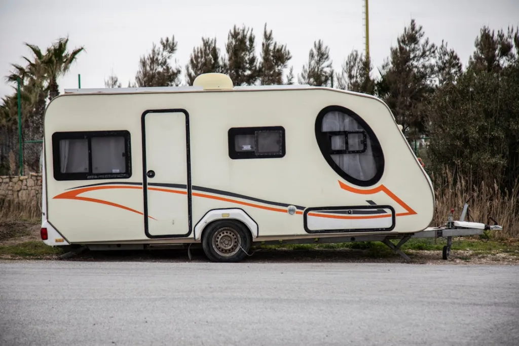 A small, white camper with orange and black accents, parked on a roadside.