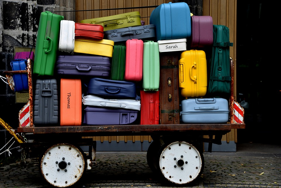 A cart stacked high with various colorful suitcases, with names written on some of them.