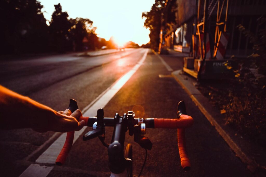 A person riding a bicycle at sunset, with an outstretched arm and the sun setting in the distance.