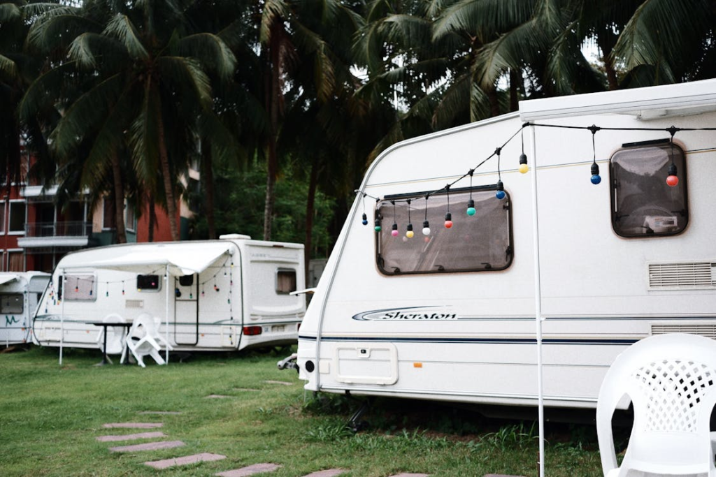 Several RVs parked in a campground area with palm trees around; a string of colorful lights is hung between the RVs.