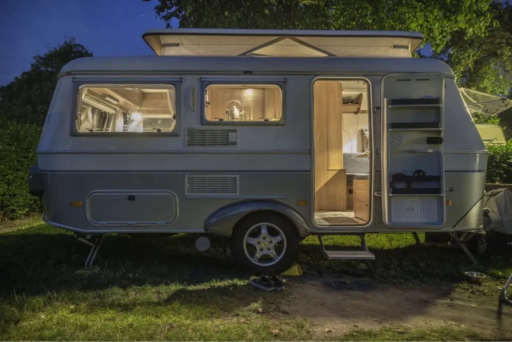 An RV illuminated from the inside, parked at night in a grassy area.