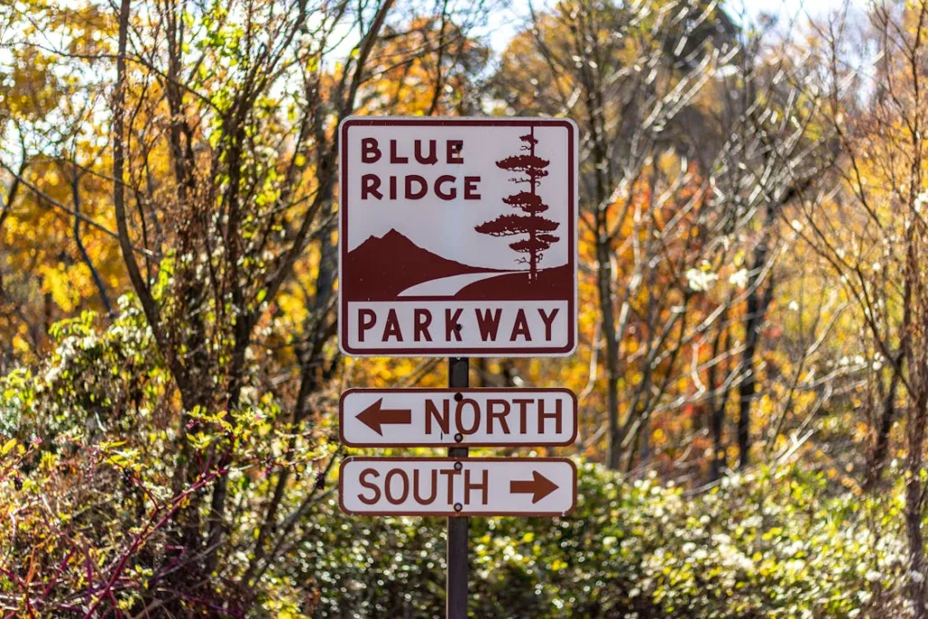 A "Blue Ridge Parkway" sign with directions pointing to North and South, with colorful autumn trees in the background.