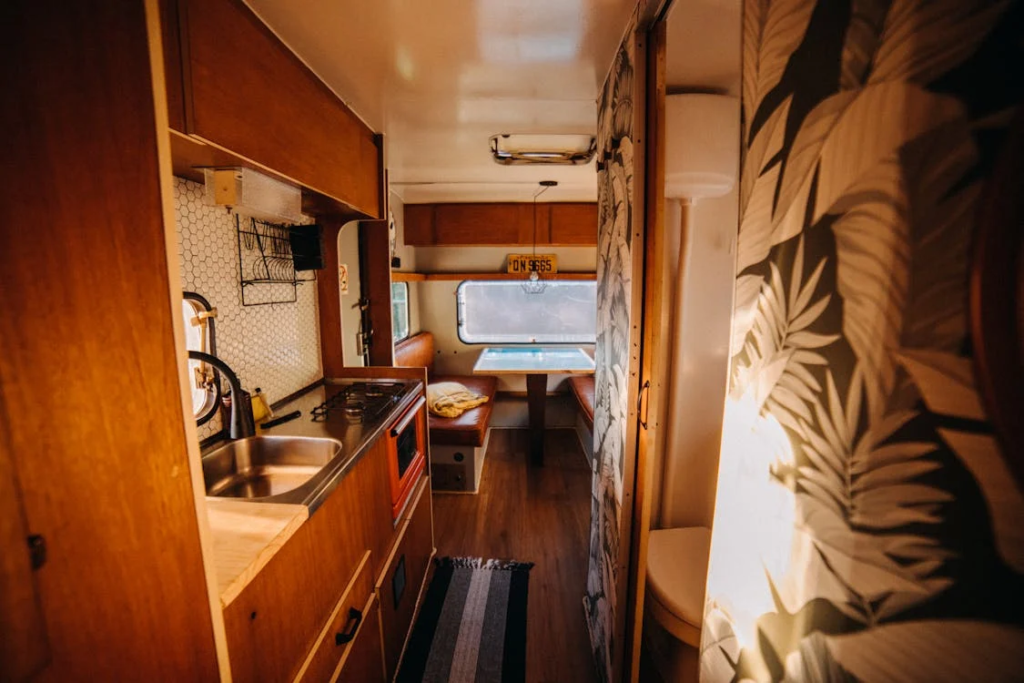 The interior view of a campervan featuring a kitchenette, dining area with a table and bench seats, and decorative wallpaper.