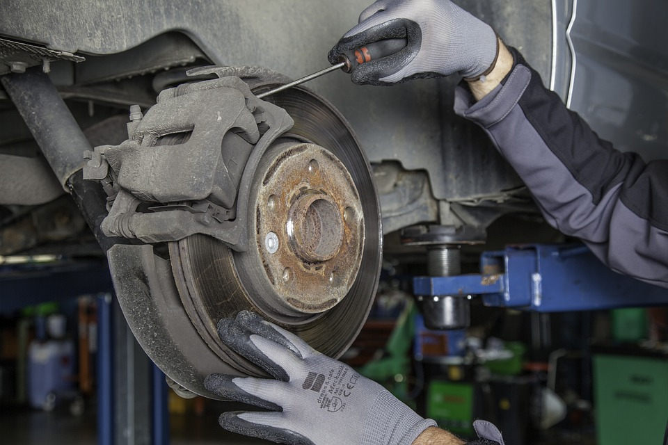 Mechanic working on a car's brake system, using a screwdriver to adjust or repair the brake components.