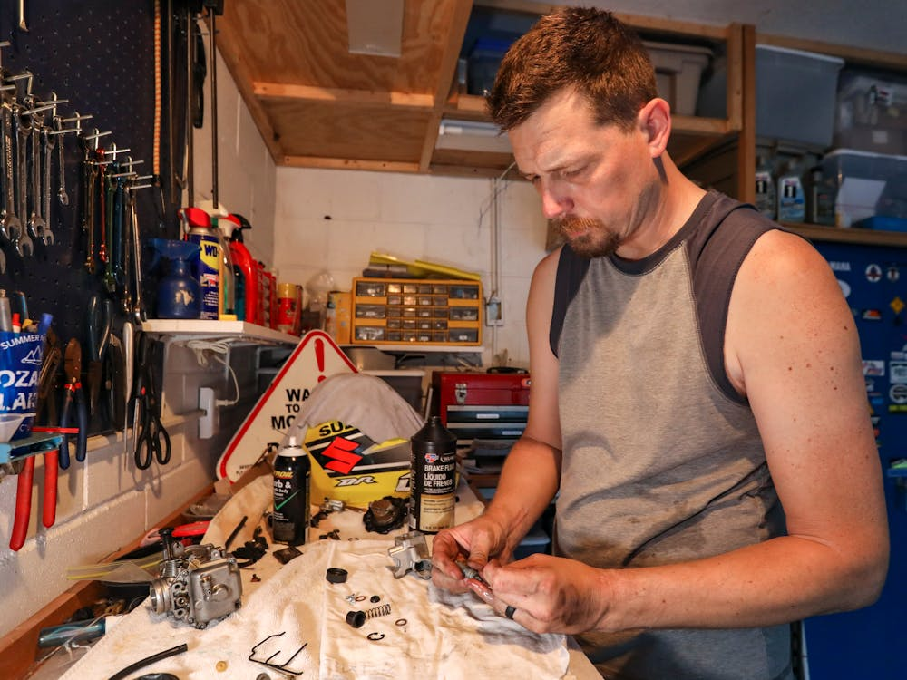  A man working in a cluttered garage, focused on a small mechanical project, with various tools and equipment around him.