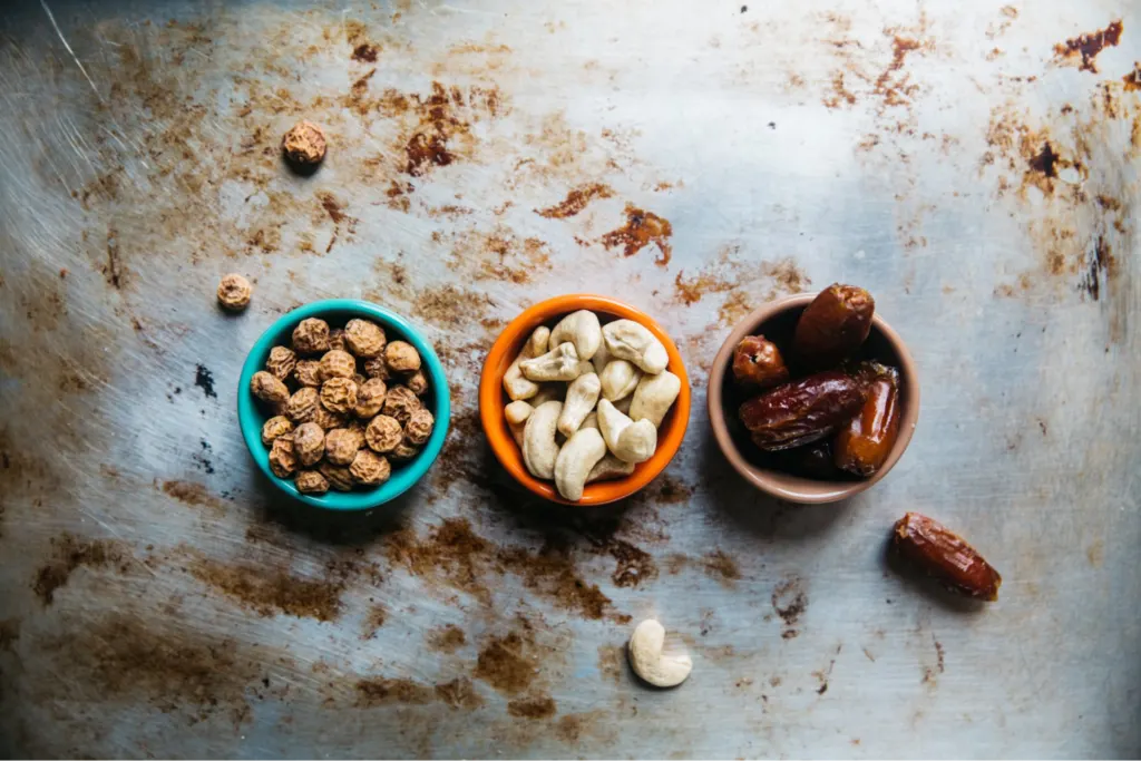 Three small bowls with different snacks: one with dried nuts, another with cashews, and the third with dates.