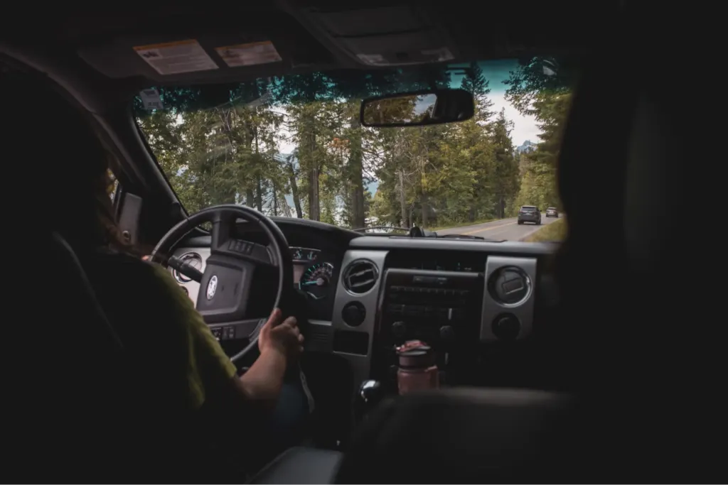 A view from inside a car of someone driving on a scenic road with trees and vehicles ahead.