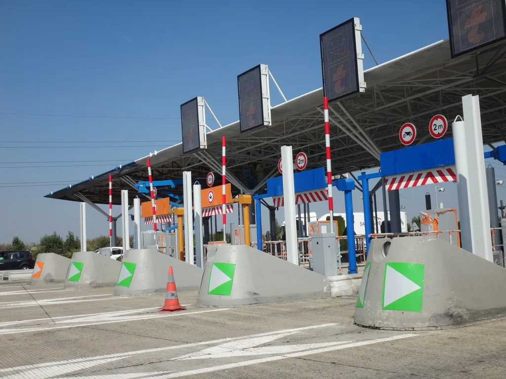 A toll booth area with multiple lanes, signs, and barriers under a clear blue sky.