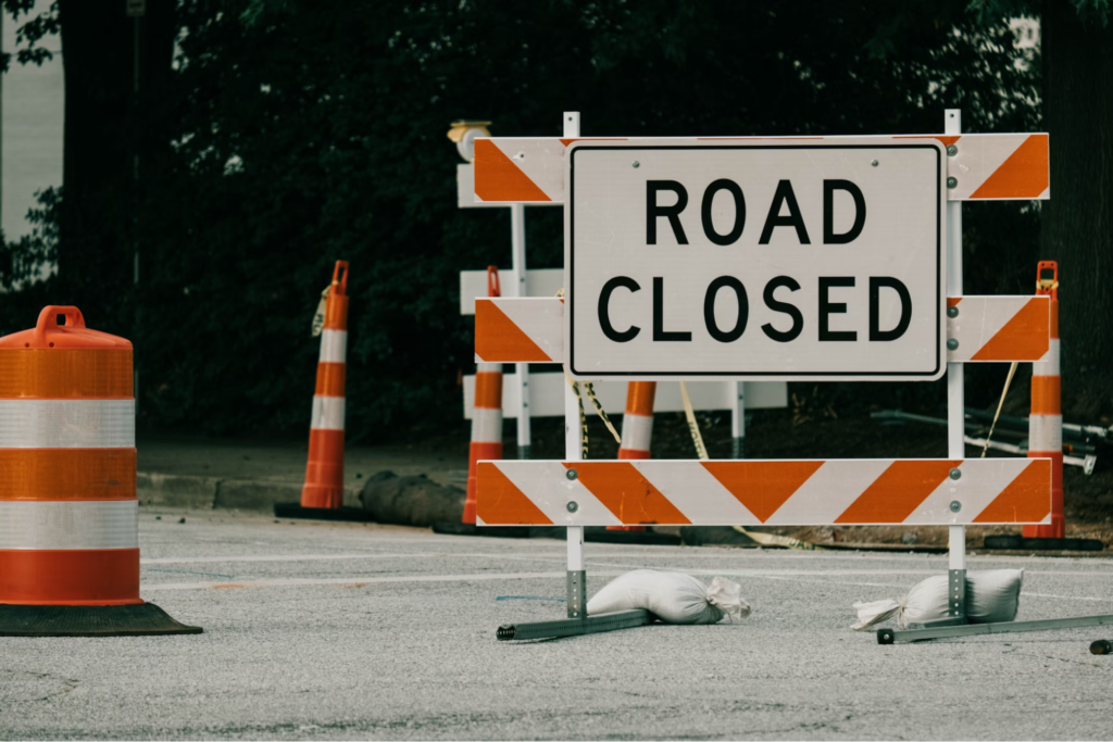 A road closed sign with barrier and traffic cones, indicating a road closure.