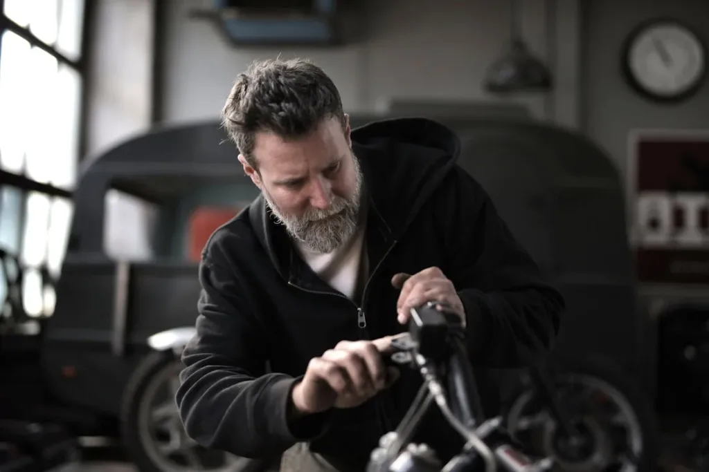 A man with a beard working in a workshop, focused on a repair task, with a blurred background.