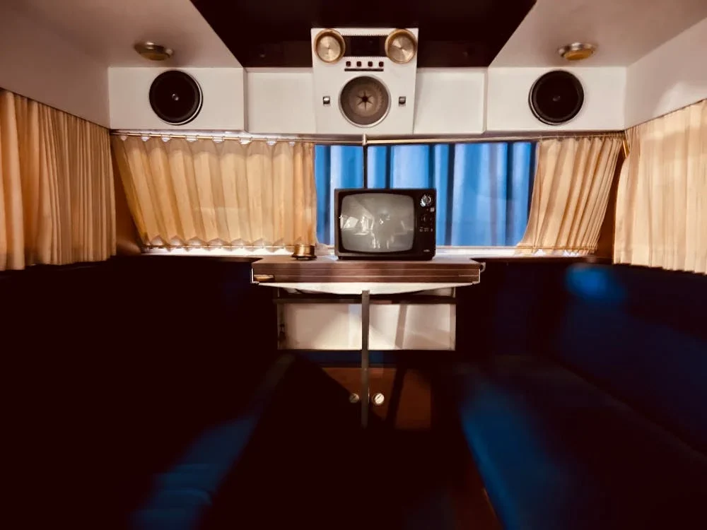 Interior of a vintage campervan with curtains, a TV, a bench, and a retro audio system.