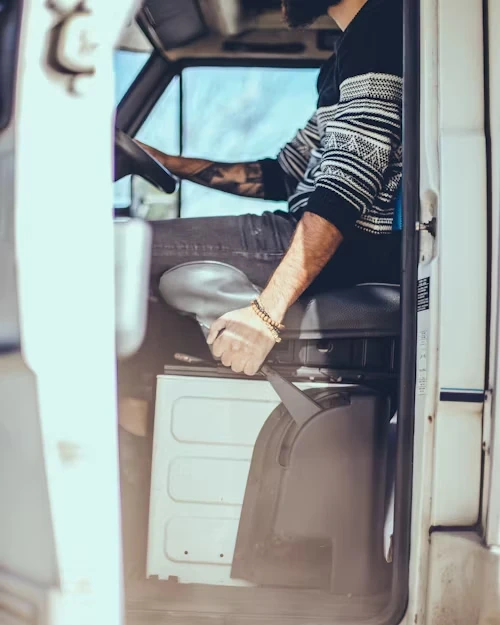 A person sitting in the driver's seat of a vehicle, seen from the side door.