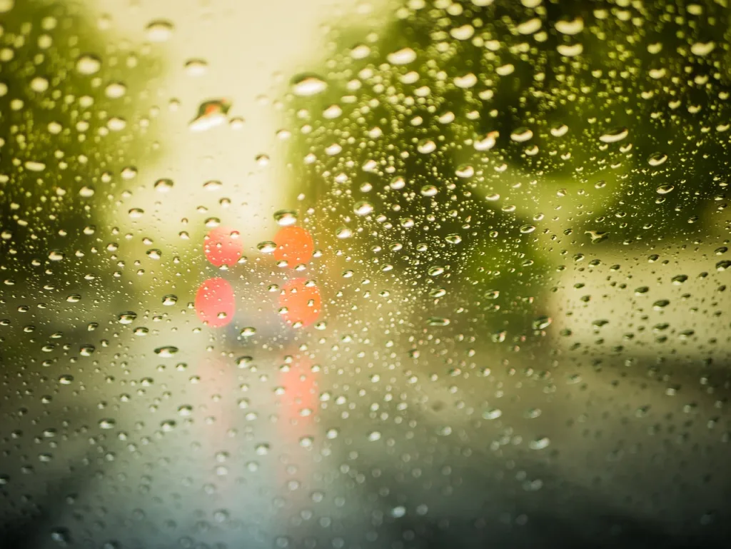 Raindrops on a car window with out-of-focus traffic lights in the background.