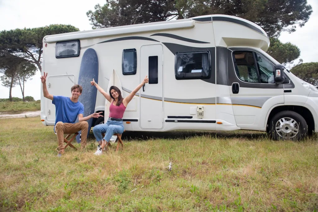 Two people sitting on chairs giving thumbs up near a motorhome, with trees in the background.