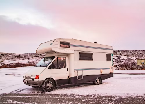 A campervan parked on a snowy road with a sunset in the background.