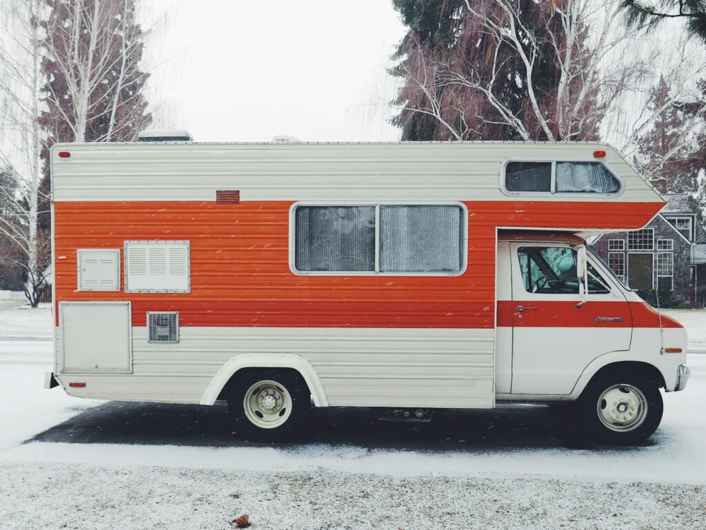 A bright and retro-styled camper van with white and orange stripes parked on a snowy roadside.