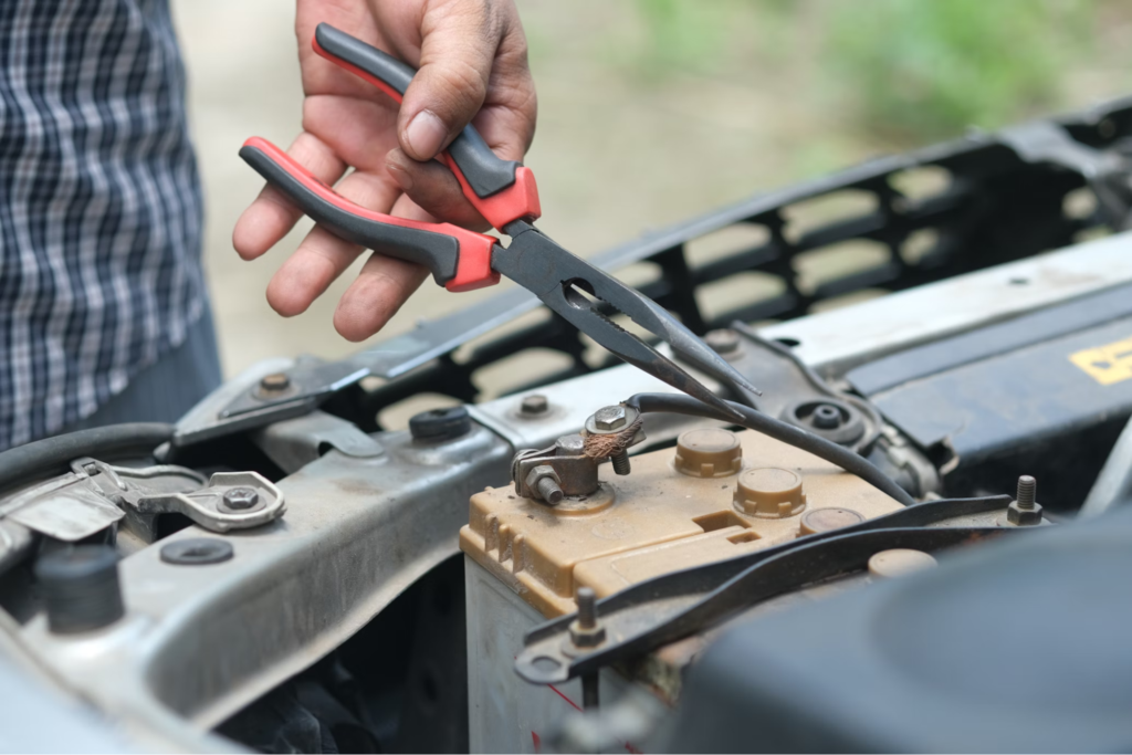 A person holding pliers and working on a car battery in the engine bay of a vehicle.