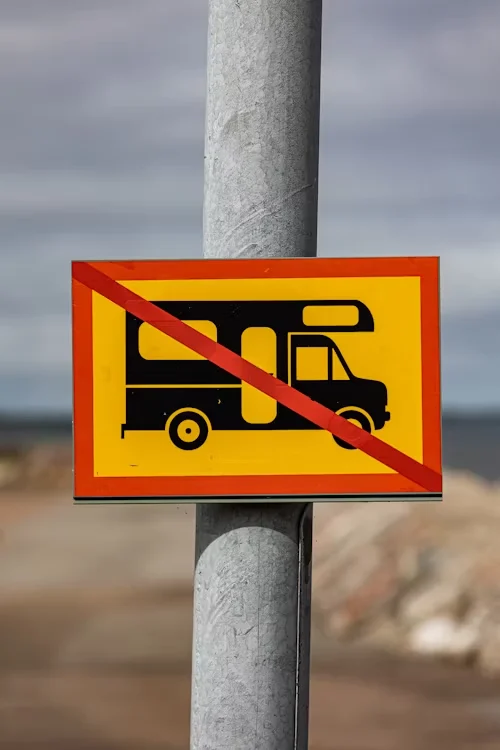 A metal pole with a sign showing a campervan with a red diagonal line through it, indicating no campervans allowed.