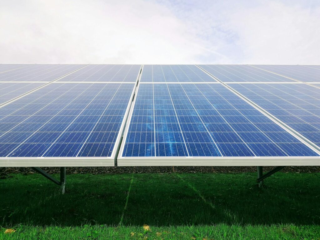 Rows of solar panels extending across a green field under a cloudy sky.