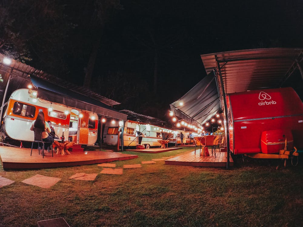 A campsite at night with several vintage travel trailers illuminated by string lights and marked with an Airbnb logo.