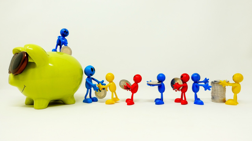 Colorful plastic figurines of people handling coins next to a large green piggy bank on a plain background.
