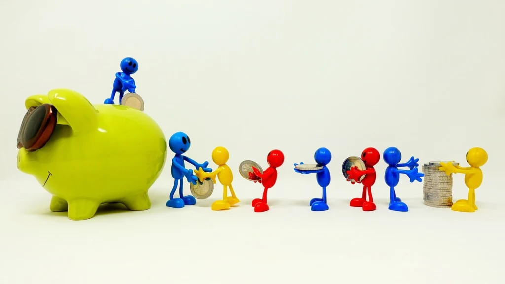 Colorful plastic figurines of people handling coins next to a large green piggy bank on a plain background.