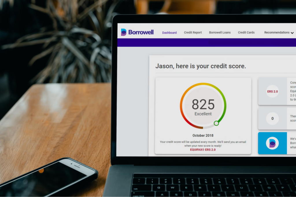 A laptop on a wooden table displaying a credit score of 825 (Excellent) on a financial website, with a smartphone placed next to it.