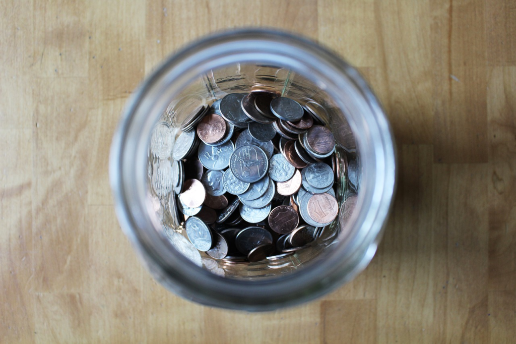 A jar filled with coins, photographed from above, placed on a wooden surface.