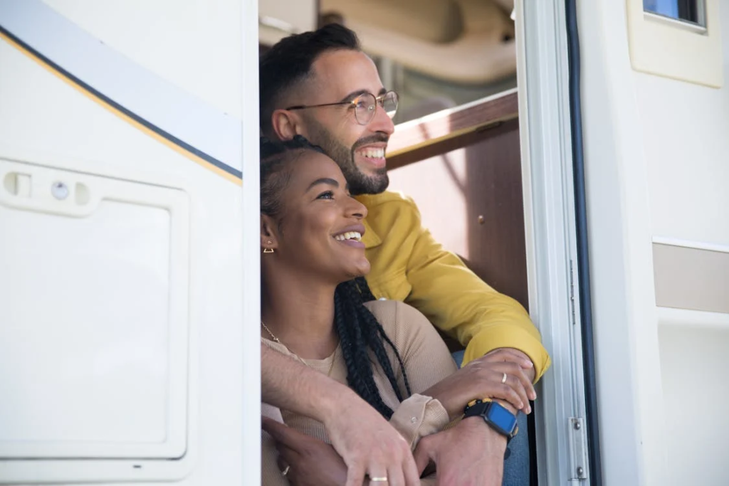 A smiling couple embracing and looking out of an RV doorway.