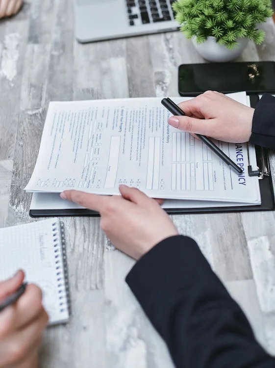 Two people reviewing an insurance policy document at a table, with a notepad, pen, plant, and smartphone nearby.