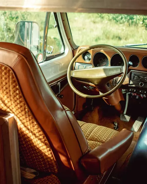 The interior view of an RV's driver's seat and steering wheel, featuring brown leather seats.