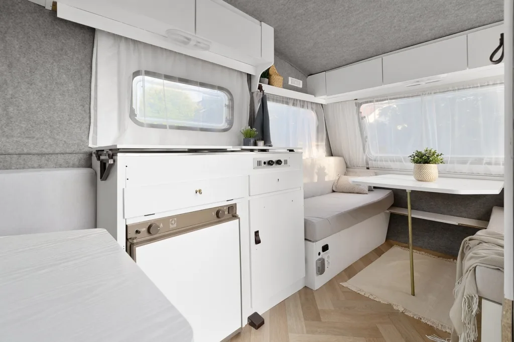 A modern and minimalist camper van interior with a small dining area, white cabinets, and a clean, organized space.