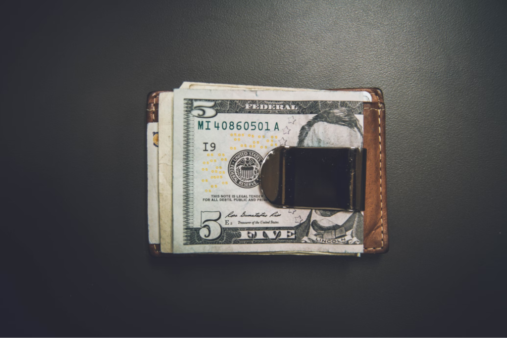 A close-up of a money clip holding several U.S. dollar bills, placed on a dark surface.
