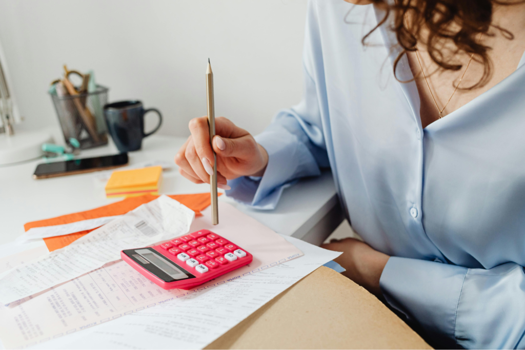 A woman using a red calculator while managing receipts and bills at a white desk.