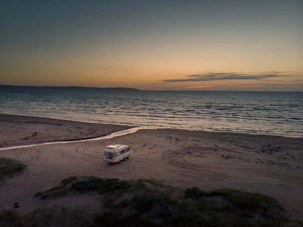 An RV parked on an empty beach near a body of water at sunset.