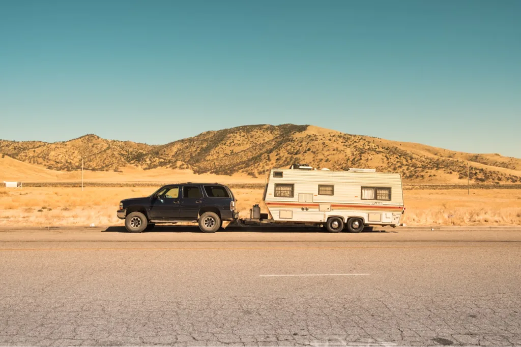 A black SUV towing a vintage travel trailer on a highway with a desert landscape in the background.