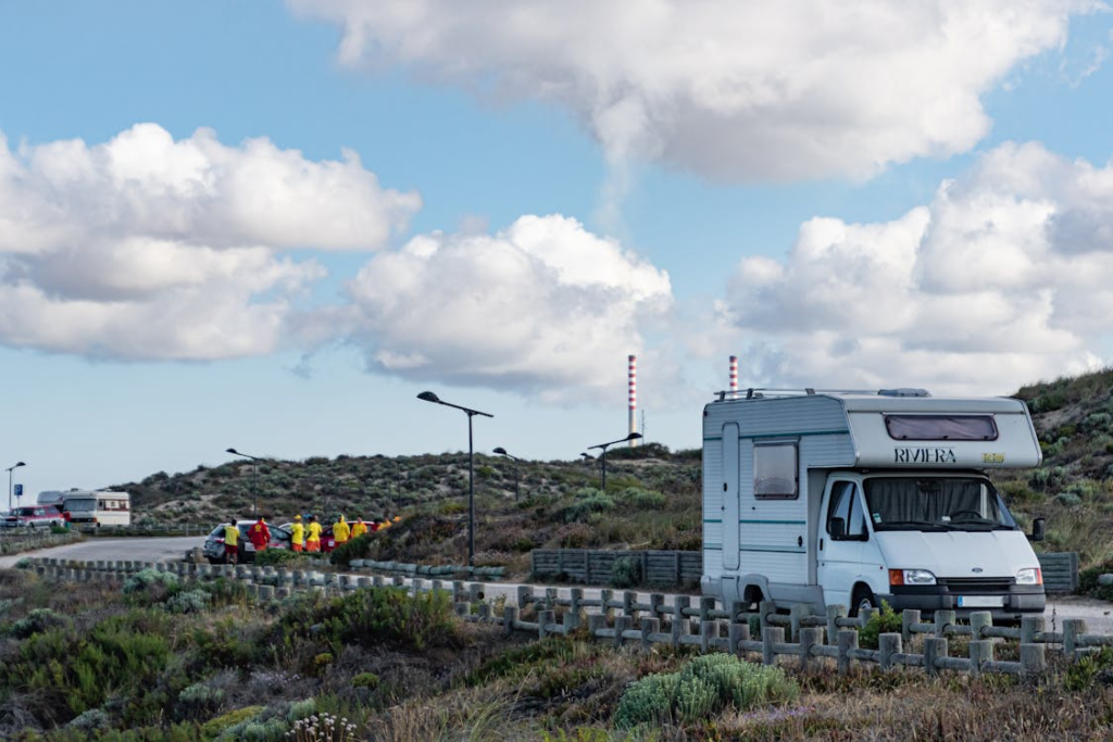 A motorhome parked on the side of a road in a hilly area, with a group of people standing by another vehicle in the background.