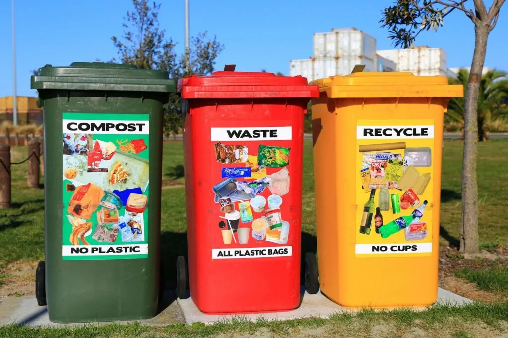 Three brightly colored trash bins labeled "Compost," "Waste," and "Recycle" in a park.